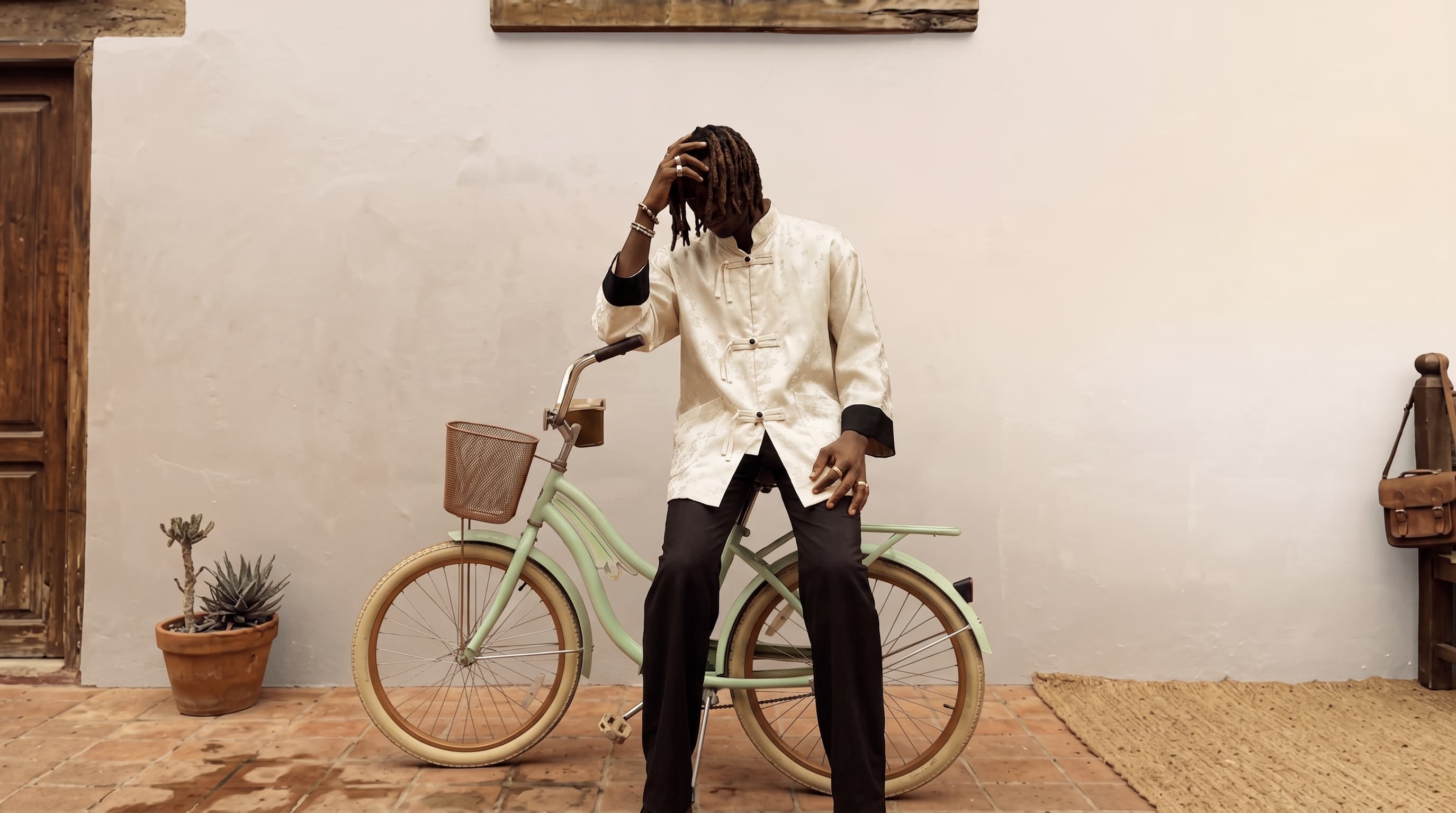 Veste jacquard ivoire portée devant un mur clair, vélo vert d'eau